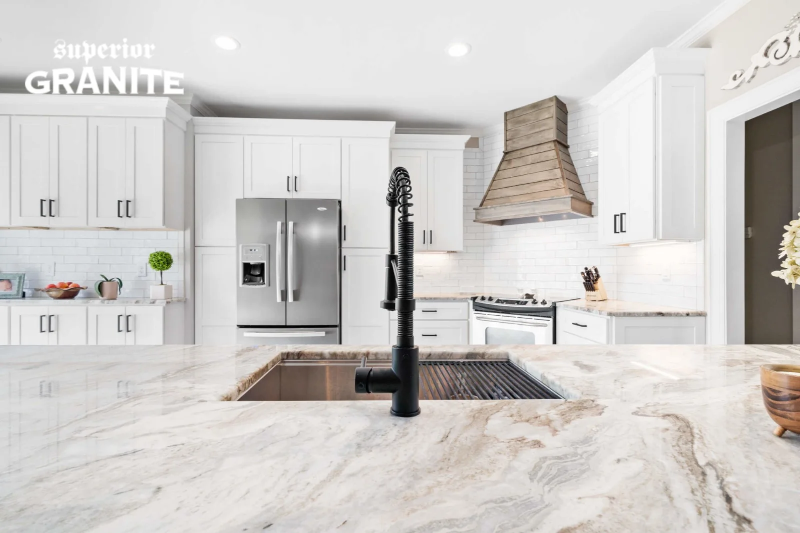 A close-up of a kitchen island featuring Fantasy Brown Marble Countertops and a black modern faucet, with a bright white kitchen in the background.