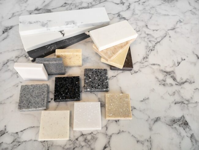 Granite vs Quartz in Coastal Florida – various stone samples including black, gray, beige, and white countertop slabs on marble surface