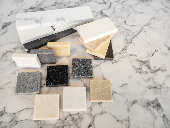 Granite vs Quartz in Coastal Florida – various stone samples including black, gray, beige, and white countertop slabs on marble surface