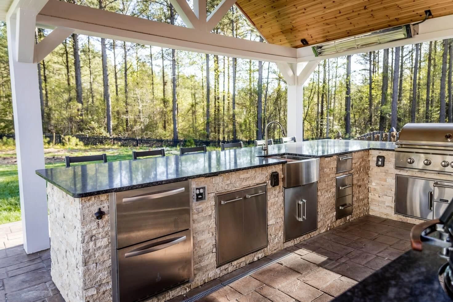 Dark stone outdoor kitchen countertops on stone island with stainless steel appliances.