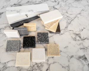 Granite vs Quartz in Coastal Florida – various stone samples including black, gray, beige, and white countertop slabs on marble surface