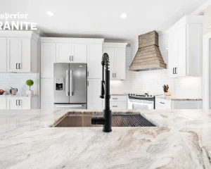 A close-up of a kitchen island featuring Fantasy Brown Marble Countertops and a black modern faucet, with a bright white kitchen in the background.
