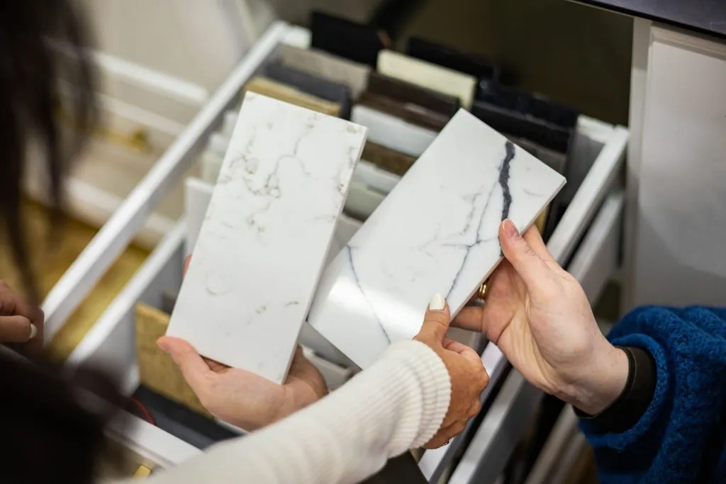 Hands holding marble sample tiles for countertop fabricator vs installer comparison.