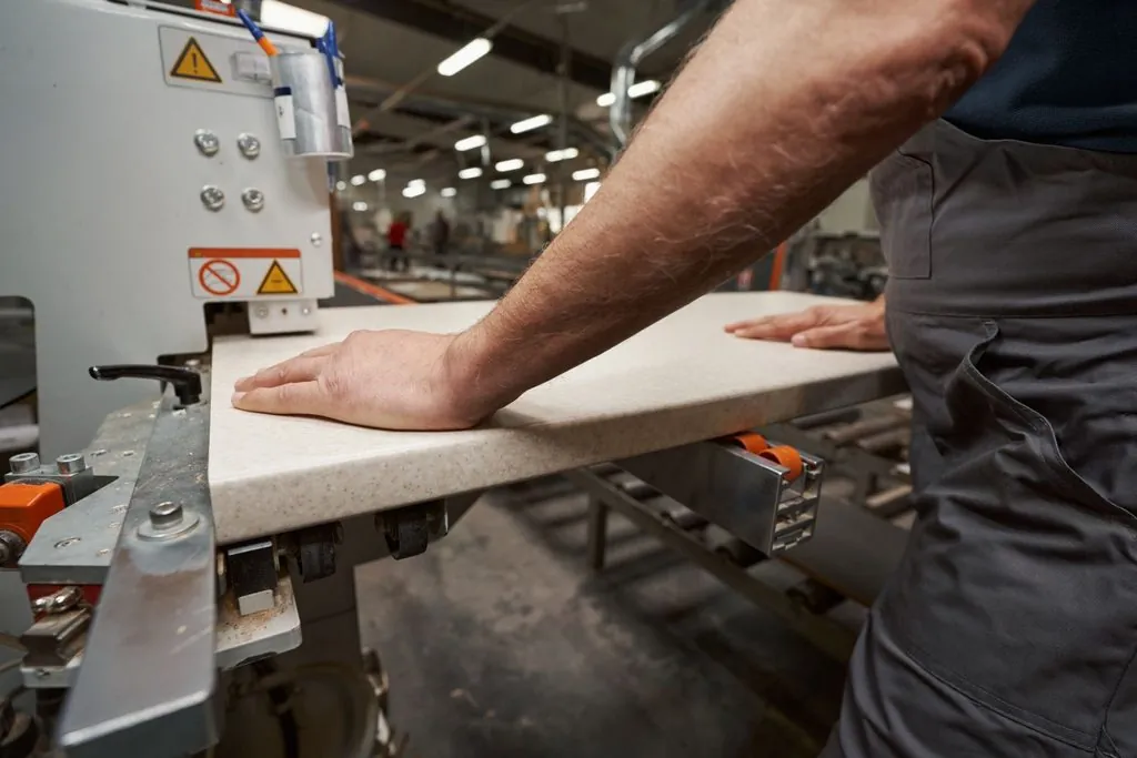 Worker operating factory slab machinery showing countertop fabricator vs installer work.